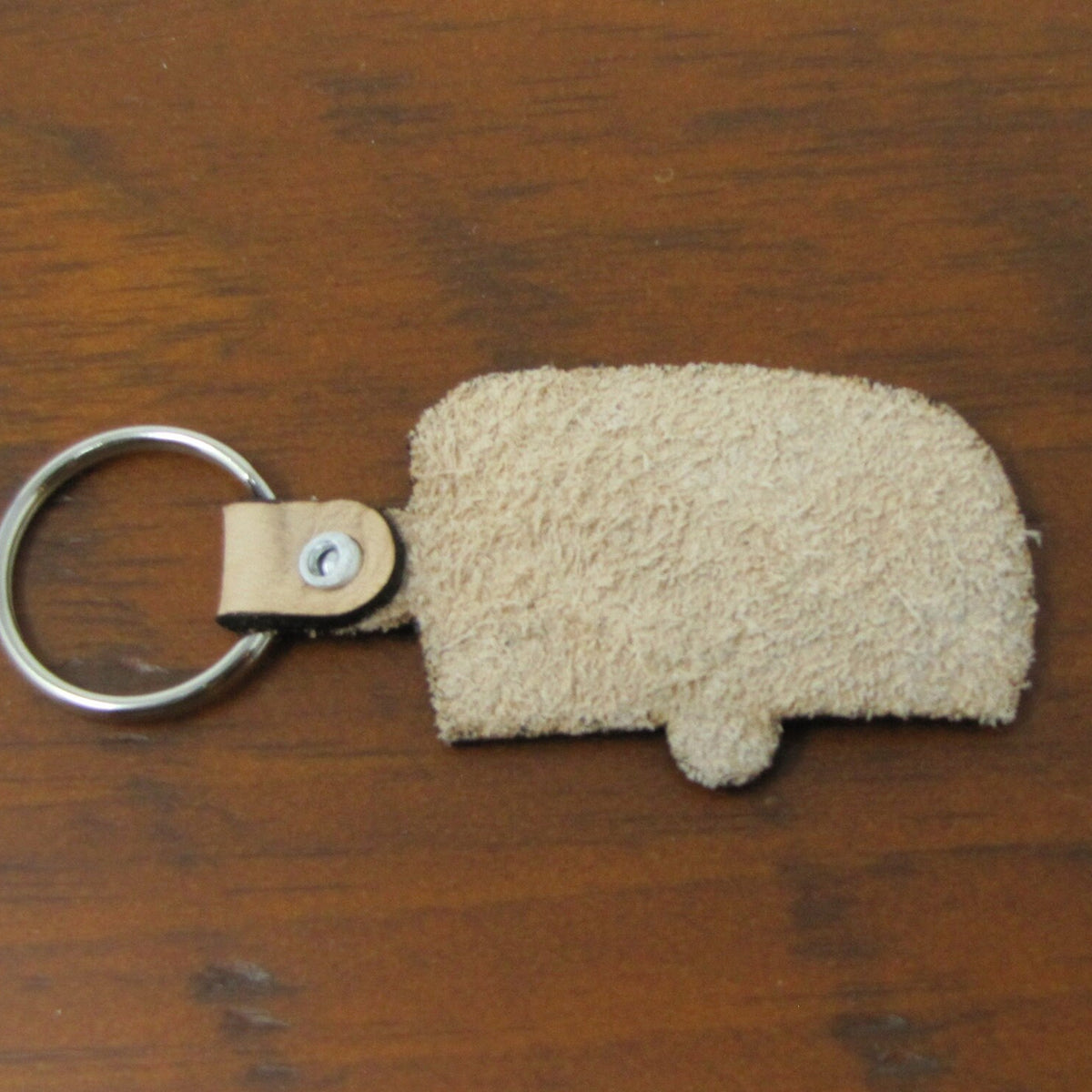 Beige keychain shaped like a camper on a wooden surface