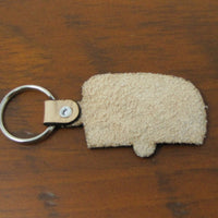 Beige keychain shaped like a camper on a wooden surface