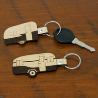 Two keychains shaped like campers on a wooden surface with a key.