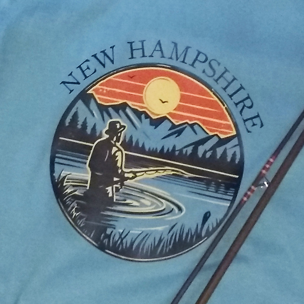 T-shirt with New Hampshire design featuring a person fishing at sunset.