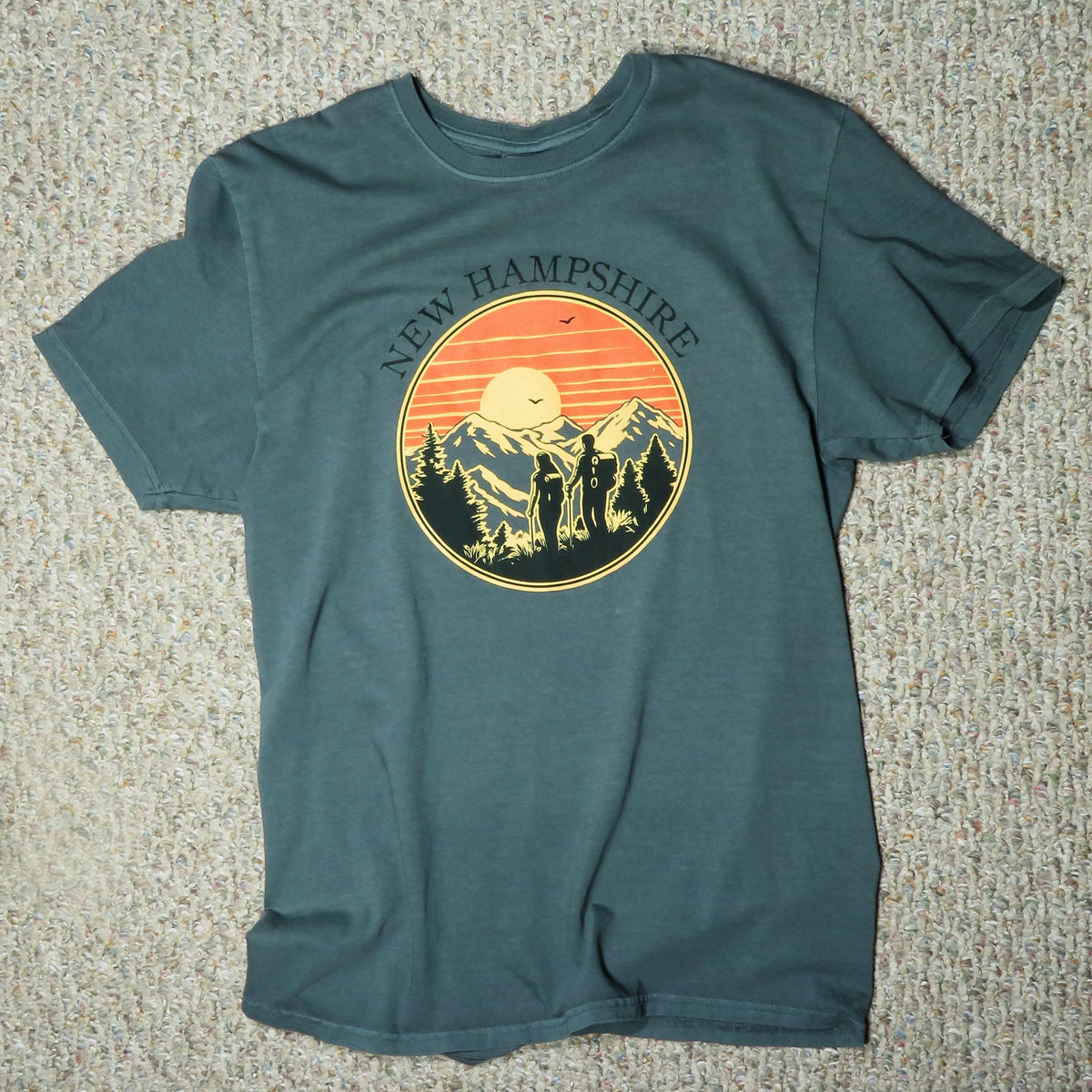 Teal t-shirt with New Hampshire graphic on a textured surface