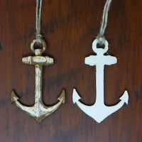Two anchor-shaped decorations, one gold and one white, hanging against a wooden background.