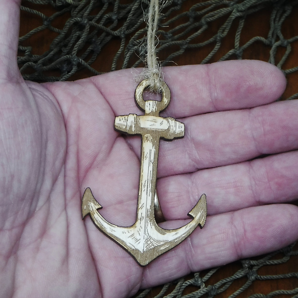 Wood anchor ornament held in a hand with fishing net in the background