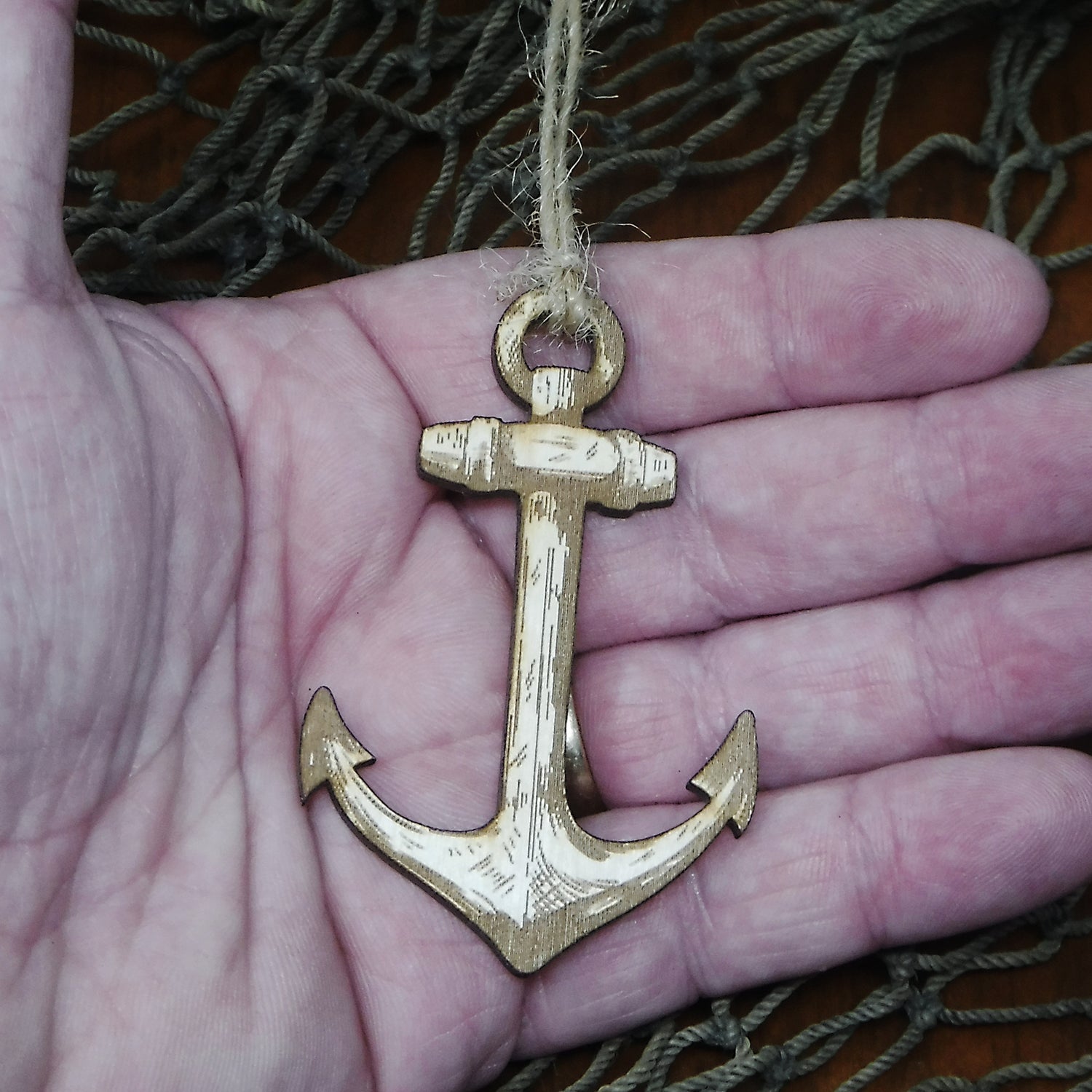 Wood anchor ornament held in a hand with fishing net in the background