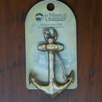 Anchor-shaped decorative item on a clear card with 'Of Moose & Mountain' branding, against a wooden background.
