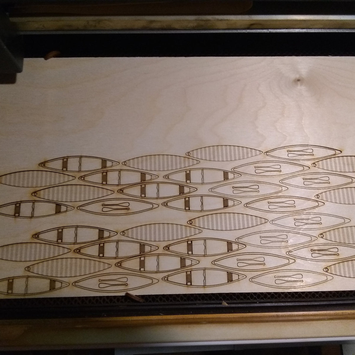 Wooden panel with laser-cut geometric patterns on a machine.