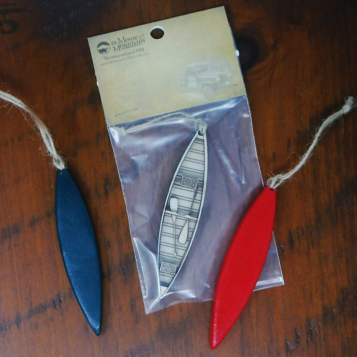 Two small boat-shaped objects, one blue and one red, with a clear plastic bag containing a white boat-shaped object on a wooden surface.
