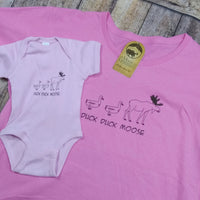Pink t-shirt and baby onesie with 'Duck Duck Moose' text and graphics on a wooden surface.