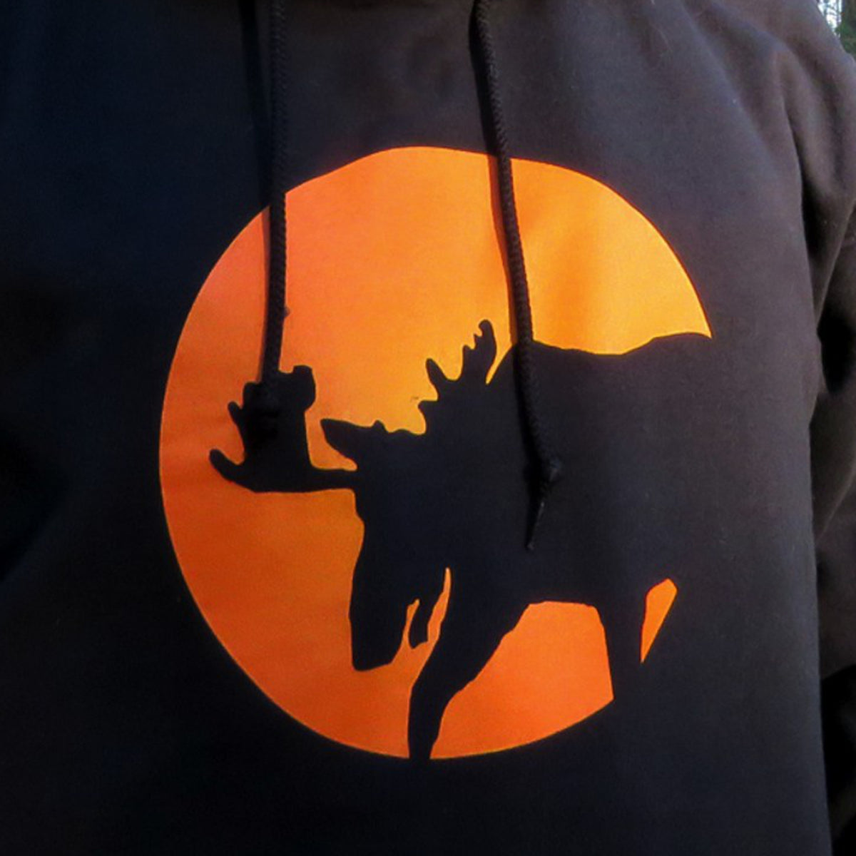 A shirt design featuring a moose silhouette in front of a full moon on a black hoodie.