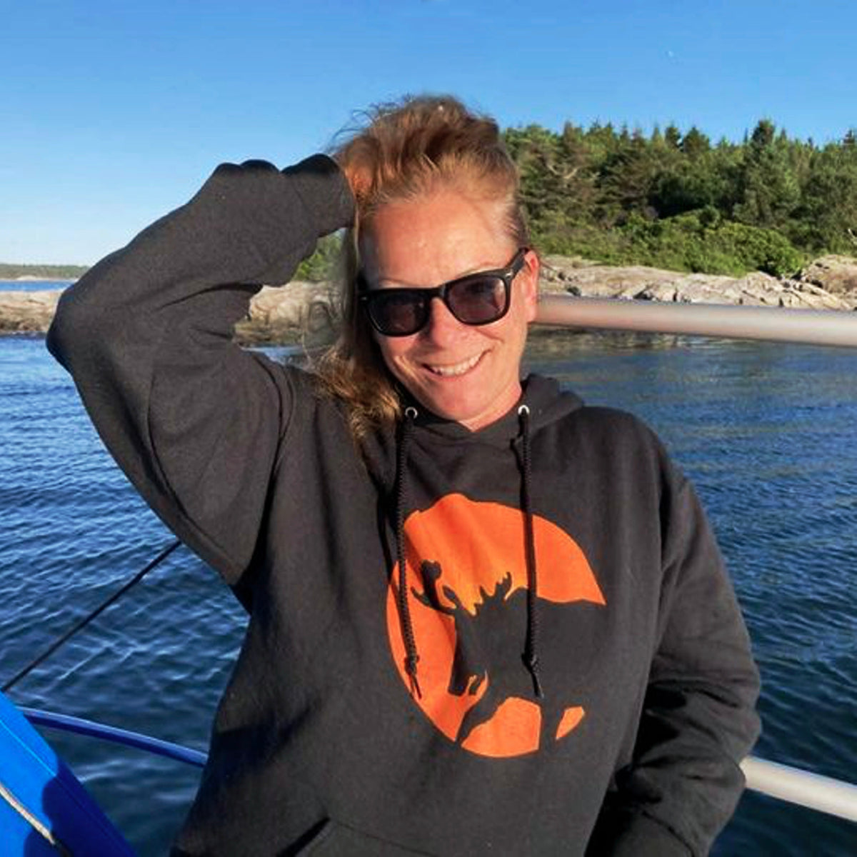 Woman wearing a hoodie with a moose and moon design by a body of water