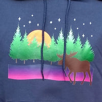 A shirt design featuring a moose in front of a row of trees as the moon rises on a stary night.