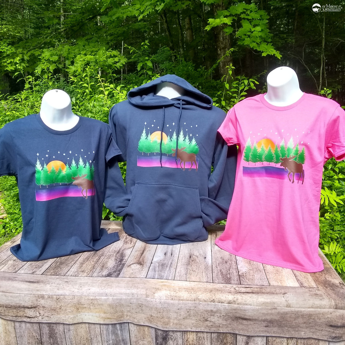 Three shirts on mannequins with nature-themed designs against a forest background