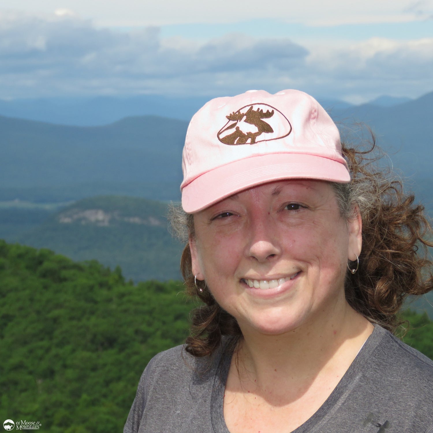 Person wearing a pink cap with a moose logo against a mountainous background
