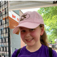 Young girl wearing a pink cap with a moose design, standing outdoors.