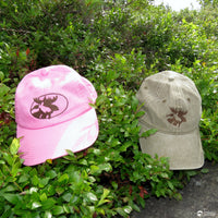 Pink and beige caps with a moose logo on green foliage