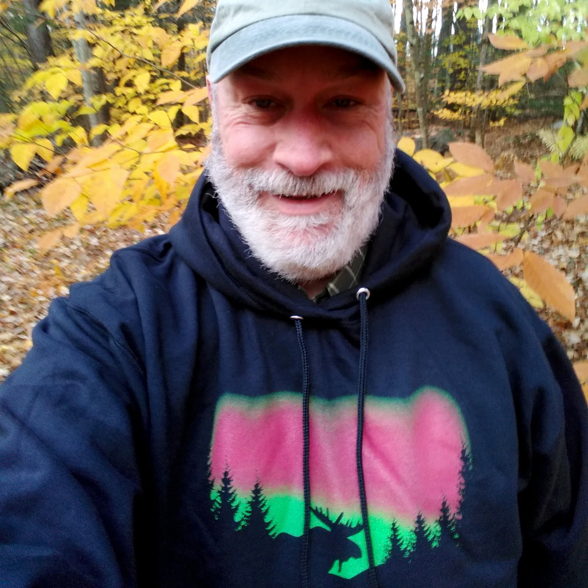 Man wearing a dark hoodie with a moose and forest and Northern Lights design in an autumn forest setting