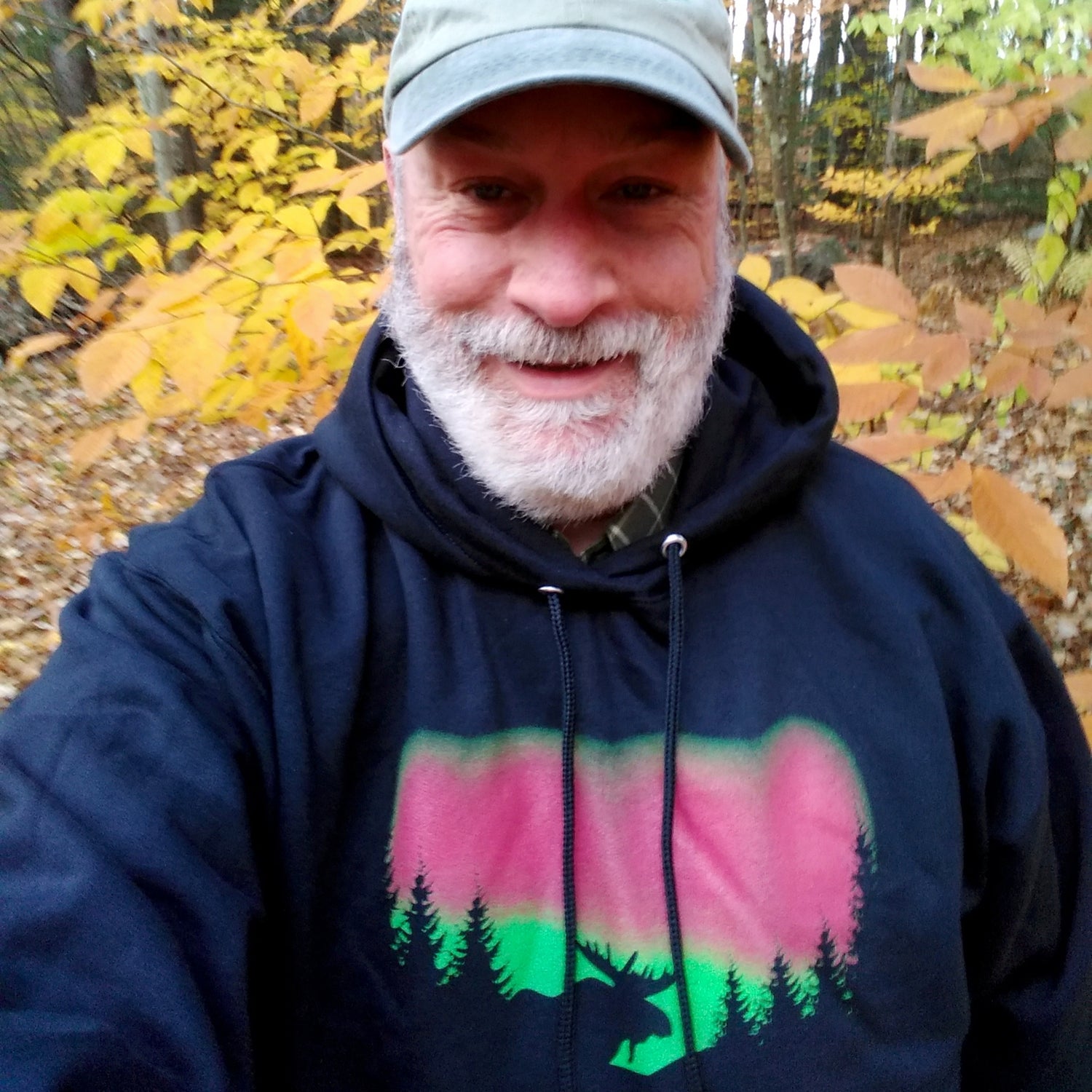 Man wearing a dark hoodie with a moose and forest and Northern Lights design in an autumn forest setting