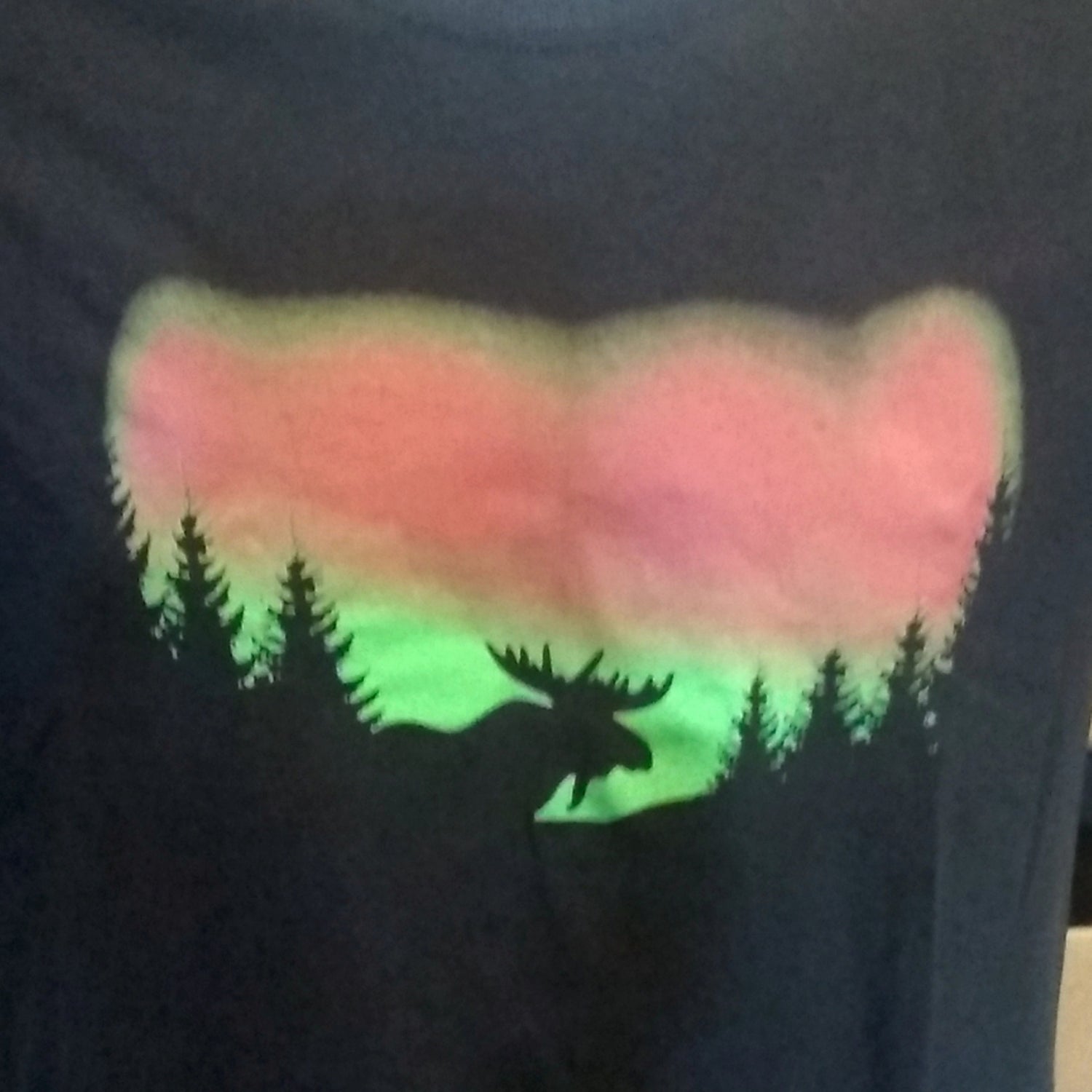 Black shirt with a moose silhouette in front of the featuring pink and green colors of the Northern Lights.