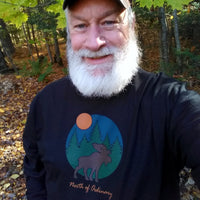 Man with a beard wearing a black shirt with a moose design in a forest setting