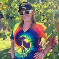 Person wearing a tie-dye shirt with a peace symbol and 'Peace Love & Moose' text, standing in a garden.