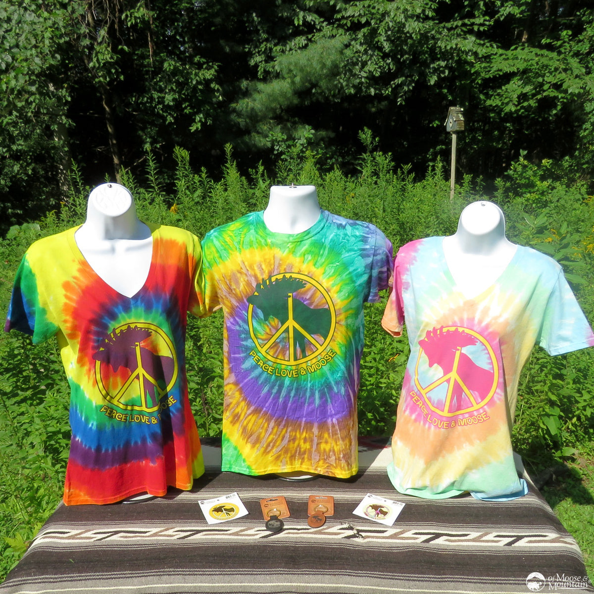 Three tie-dye t-shirts with peace symbols on mannequins outdoors.