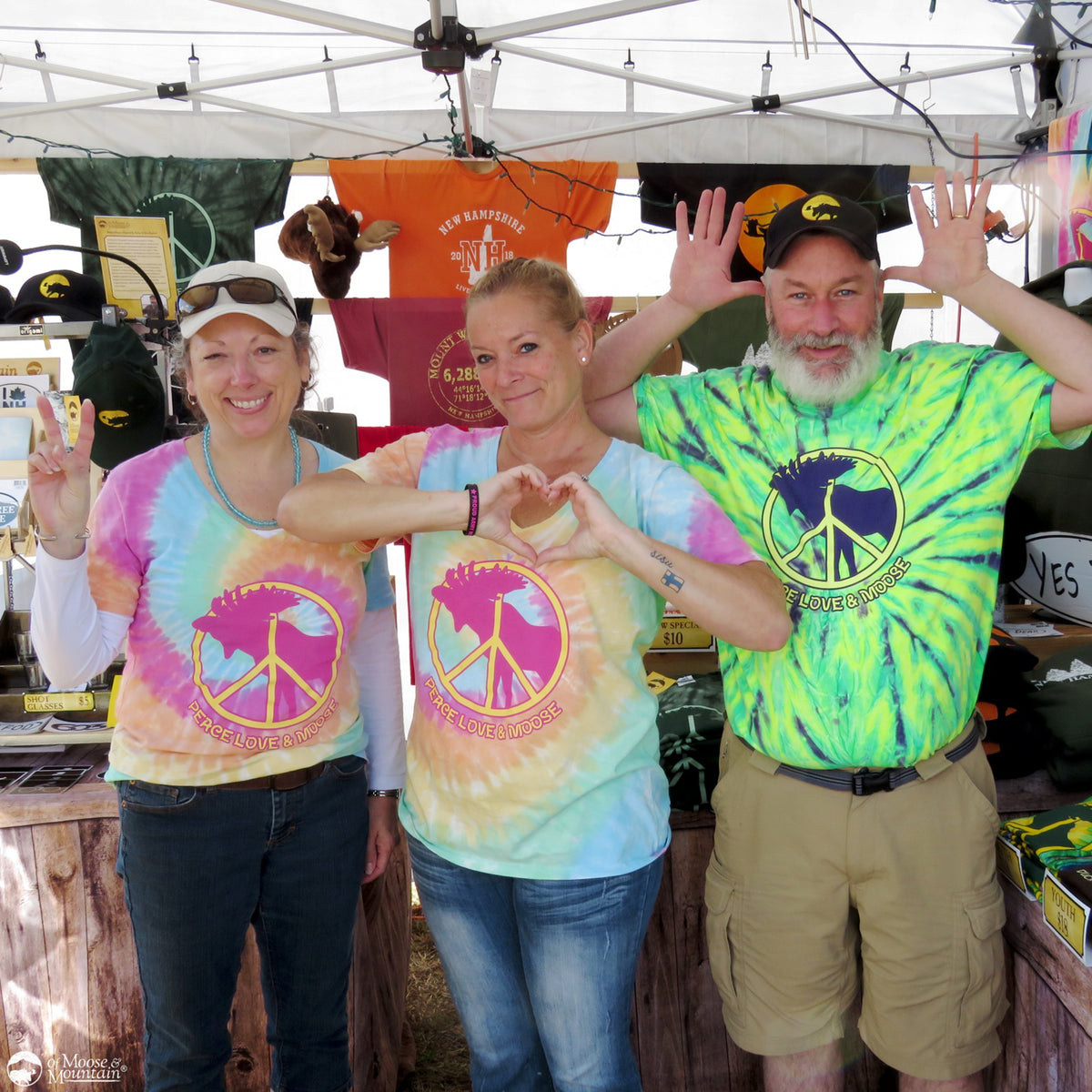 Three people wearing tie-dye shirts with peace signs at an outdoor event.