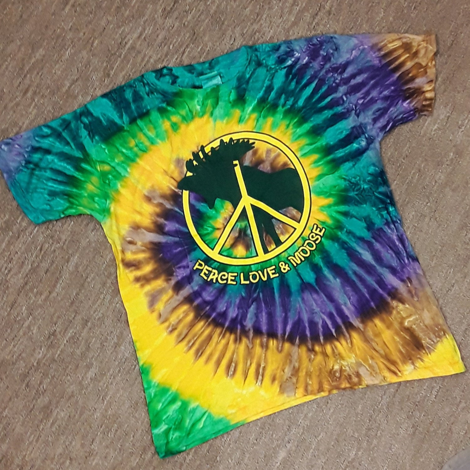 Tie-dye t-shirt with peace symbol and 'Peace Love & Moose' text on a wooden surface