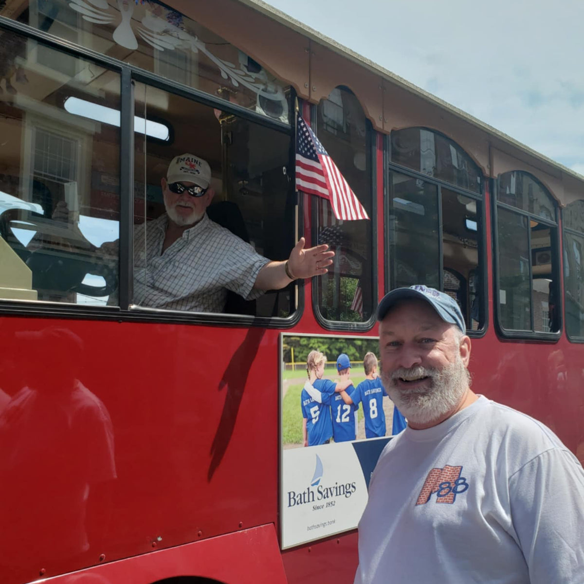 Man standing next to a red bus with a poster of people in sports jerseys and an American flag.