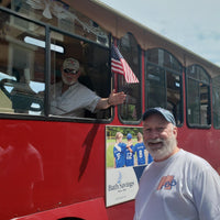 Man standing next to a red bus with a poster of people in sports jerseys and an American flag.