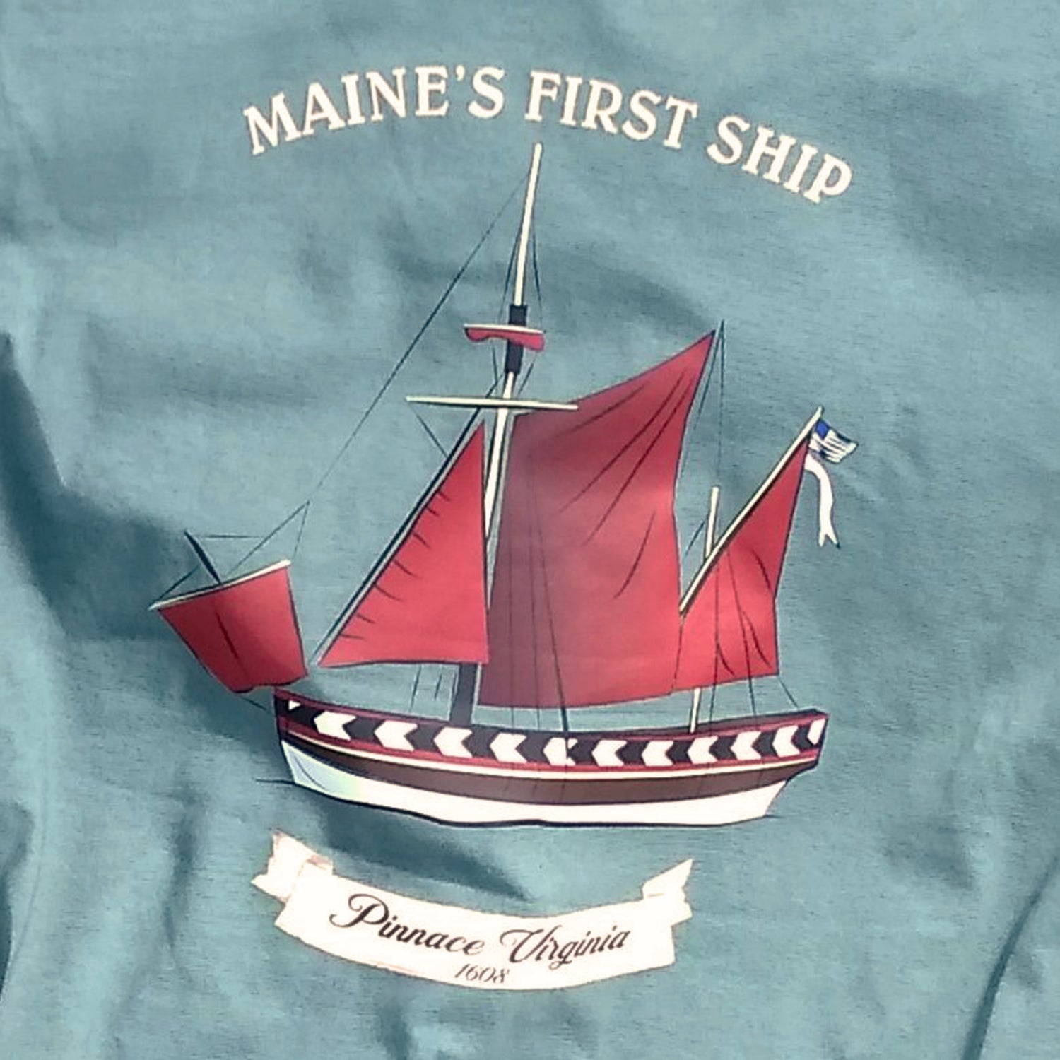 T-shirt with a ship design and 'Maine's First Ship' text on a Nordic green background