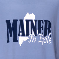 Blue t-shirt with 'MAINER In Exile' text and outline on a light blue background