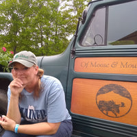 Woman sitting next to a vintage truck with 'Of Moose & Moon' branding