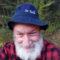 Man wearing a blue 'Maine in Exile' bucket hat and red plaid shirt outdoors.