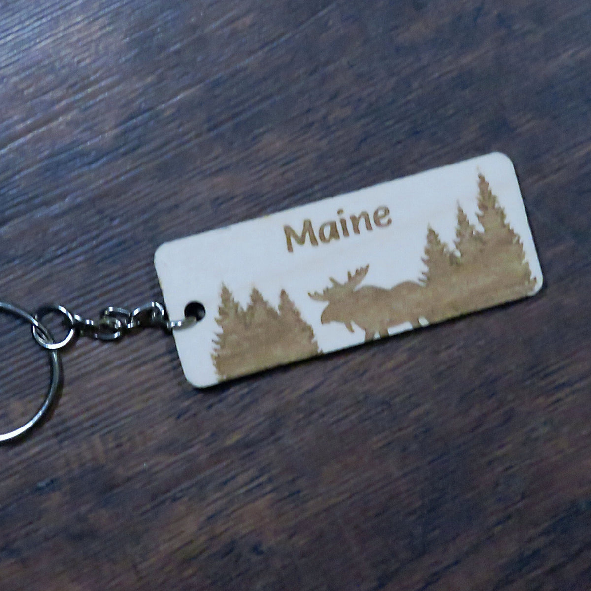 Keychain with 'Maine' and moose design on a wooden surface