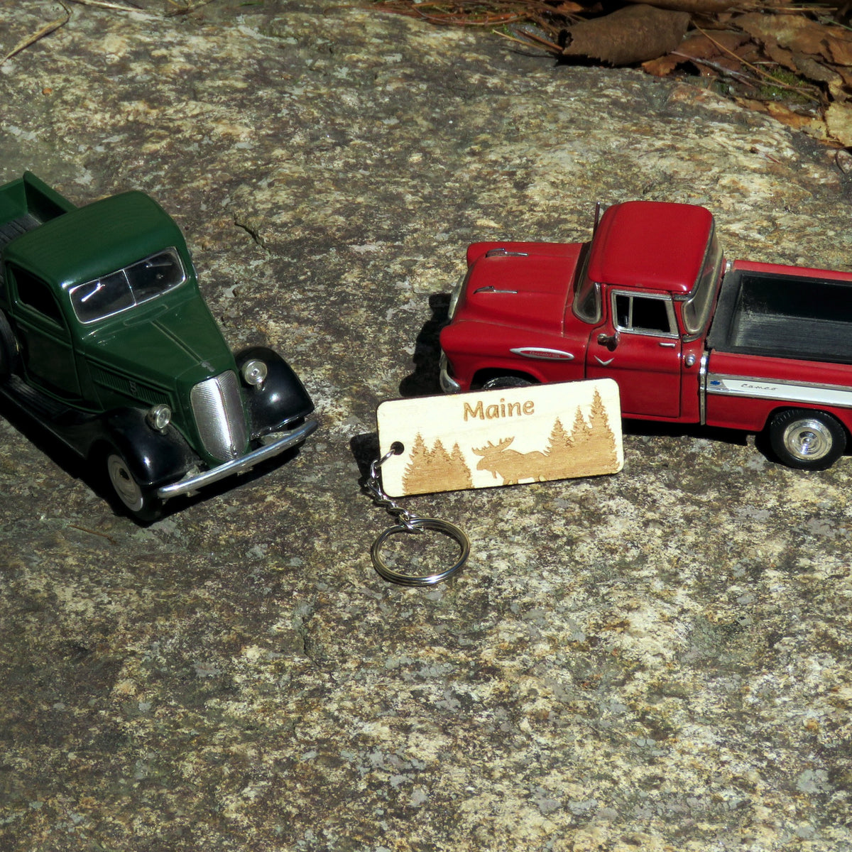 Two toy trucks and a keychain with 'Maine' on it on a textured surface.
