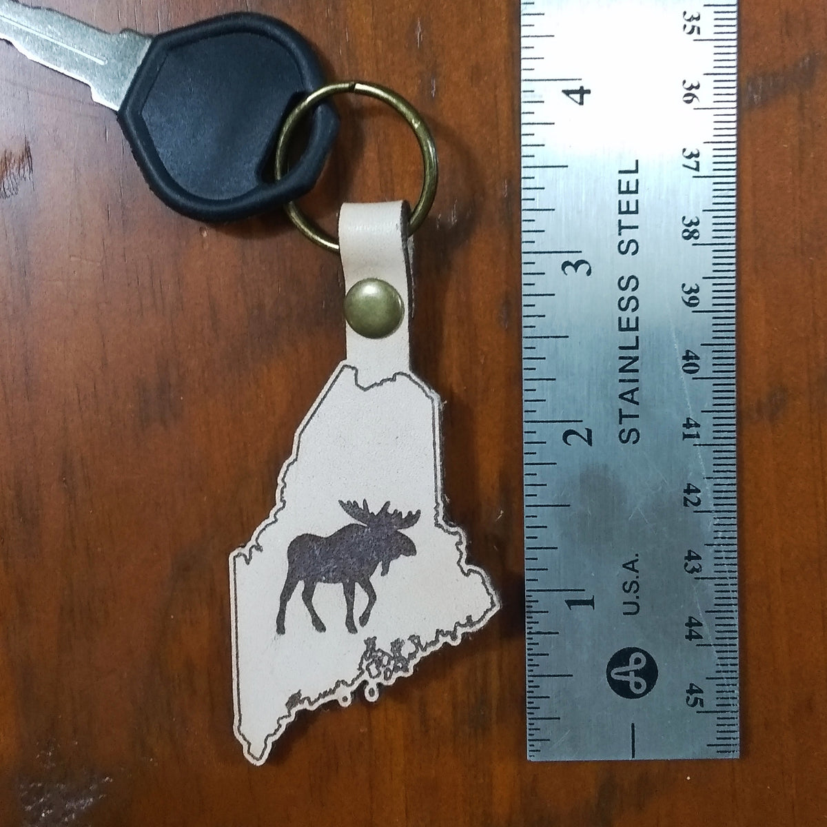 Keychain with moose design on a state outline next to a ruler on a wooden surface