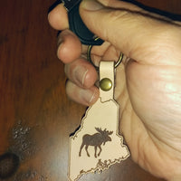 Hand holding a keychain with a moose design on a leather state outline