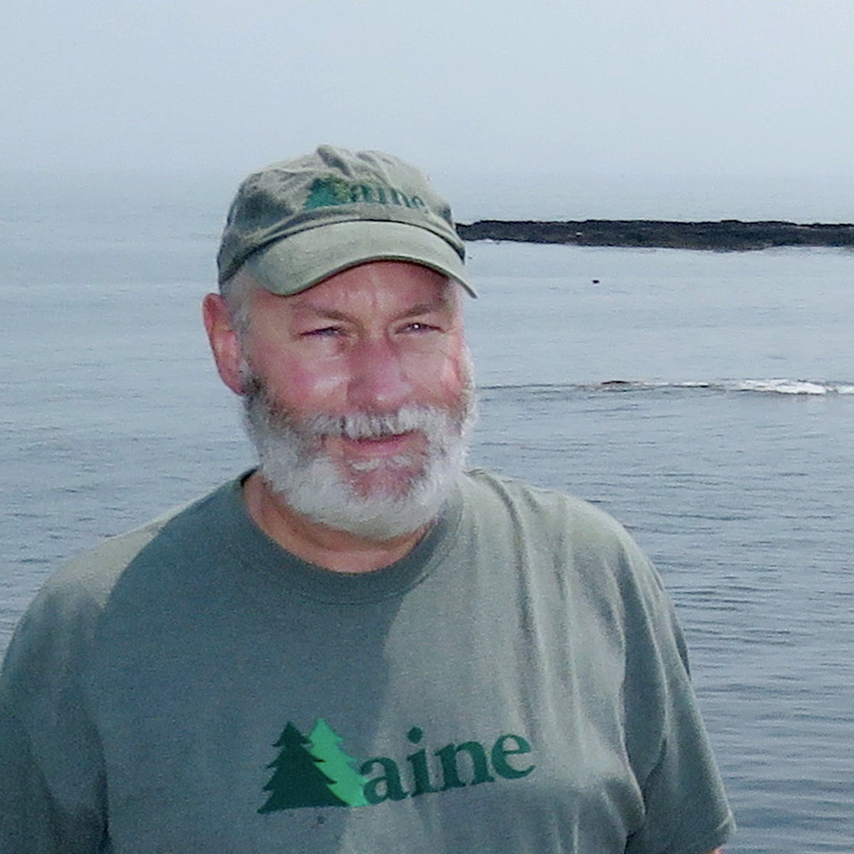 Man wearing a cap and 'Maine' t-shirt by a body of water