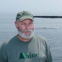 Man wearing a cap and 'Maine' t-shirt by a body of water