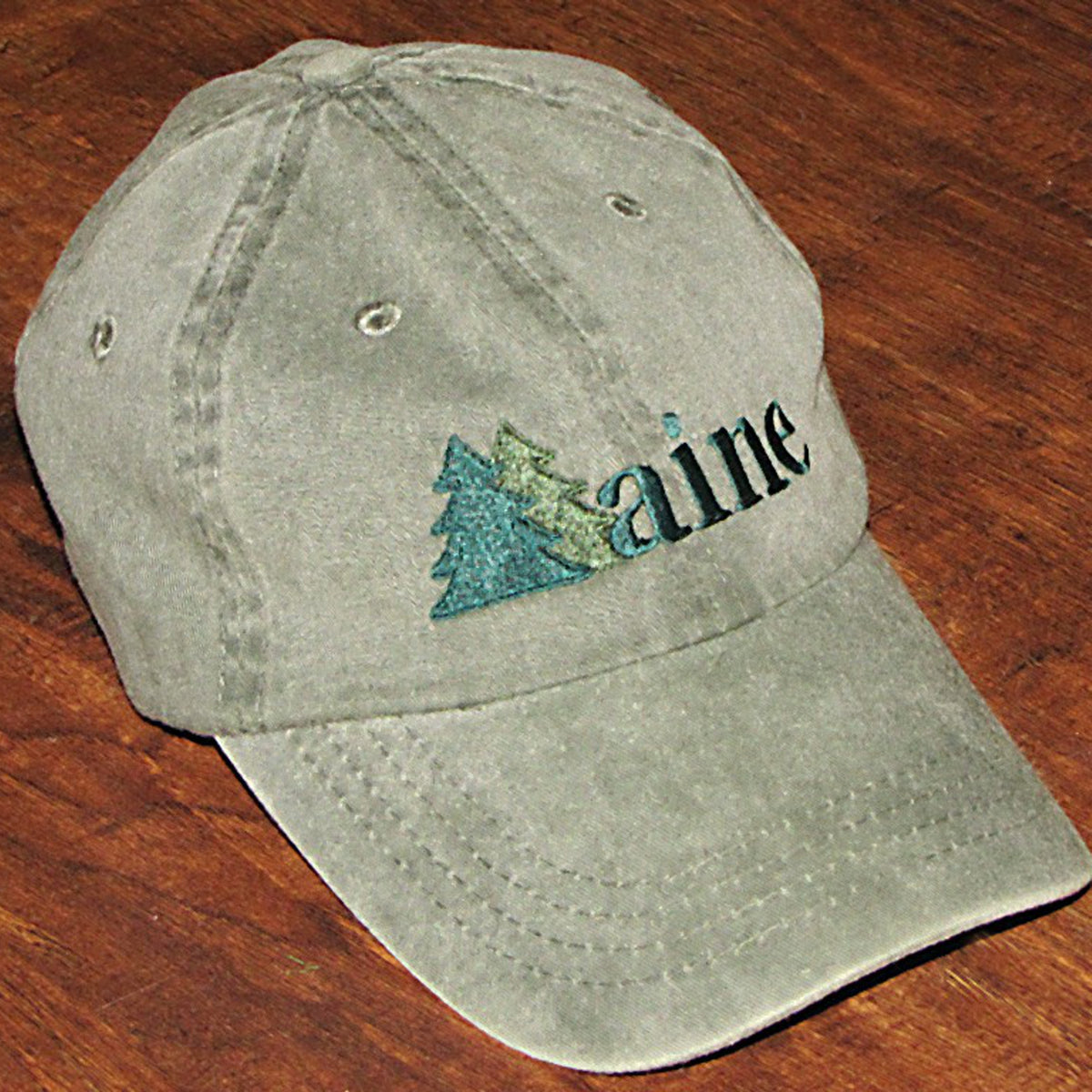 Green cap with 'Maine' and two trees design on a wooden surface