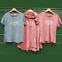 Two pink t-shirts and a gray t-shirt with 'Maine' design on hangers against a green background