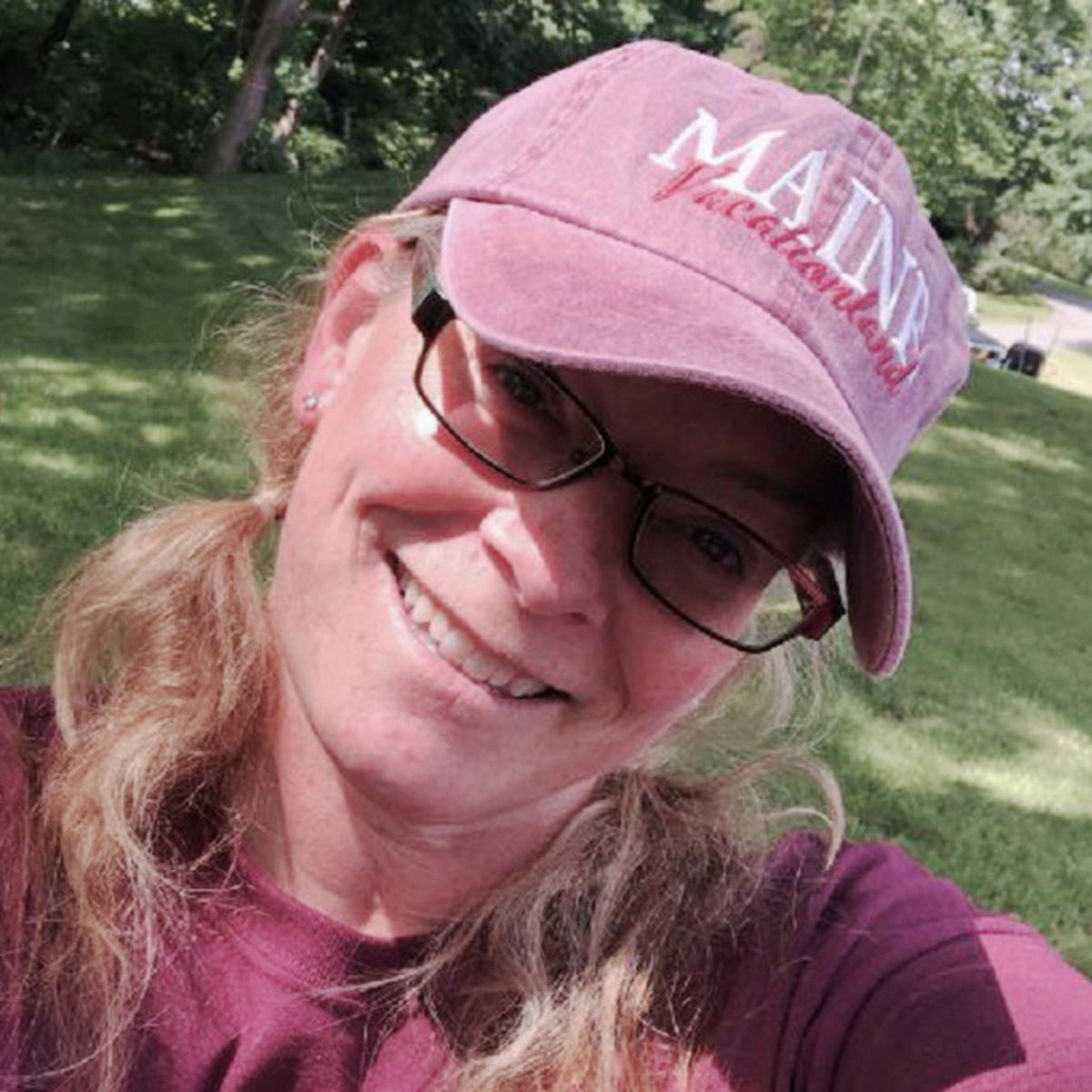 Woman wearing a maroon cap with 'Maine' printed on it, outdoors.