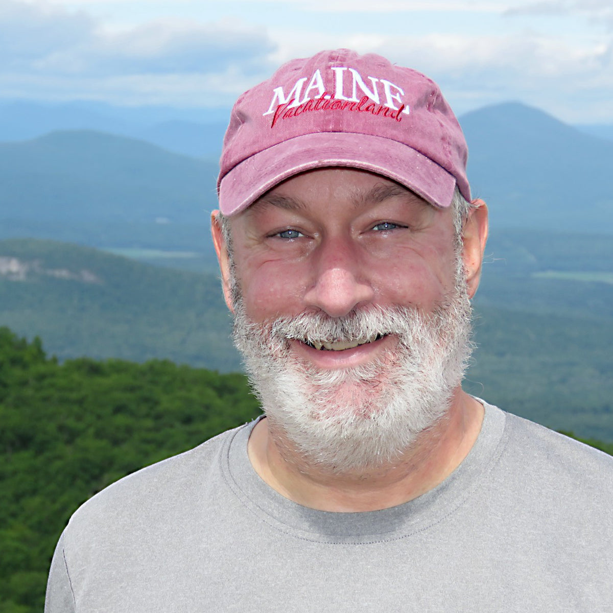 Man wearing a maroon 'MAINE' cap with mountains in the background