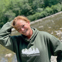 Person wearing a green 'New Hampshire' hoodie by a river