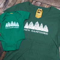 Green t-shirt and baby onesie with 'New Hampshire' design on a wooden surface