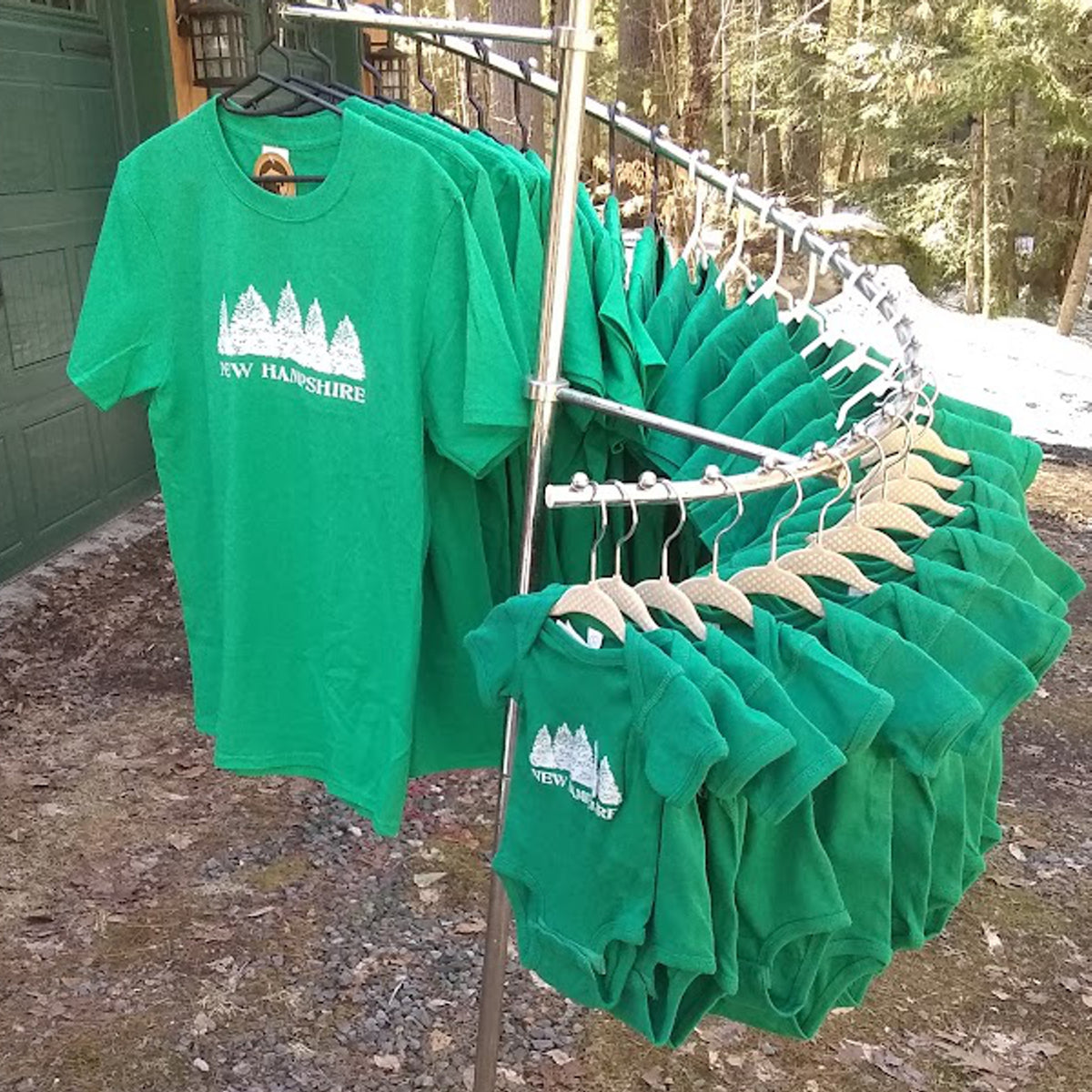 Green t-shirts with 'New Hampshire' print on hangers outdoors.