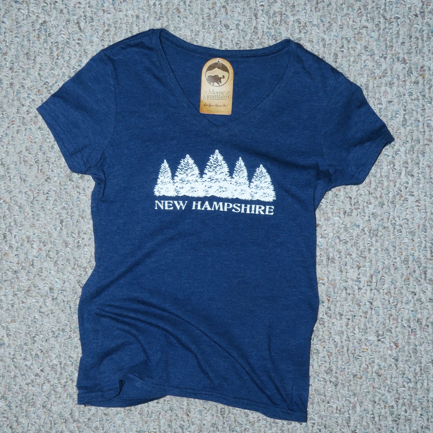 Blue t-shirt with 'New Hampshire' and tree design on a textured surface