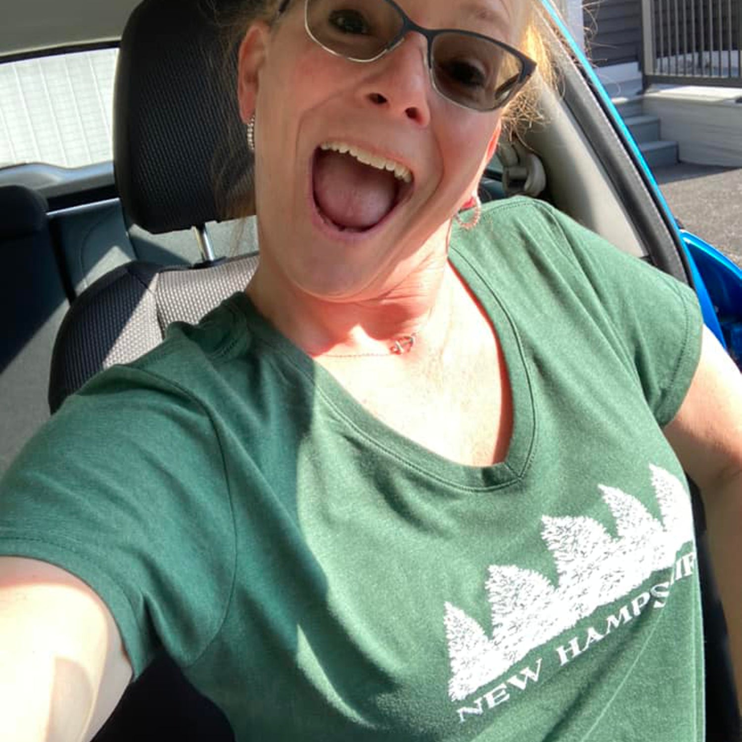 Person wearing a green 'New Hampshire' t-shirt with a row of evergreen trees inside a vehicle