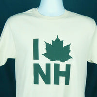 White t-shirt with green maple leaf and 'I ❤️ NH' text on a mannequin against a dark blue background