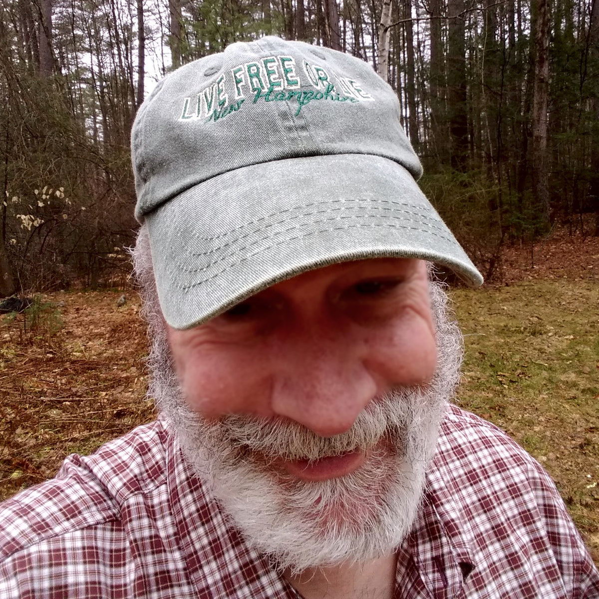 Man wearing a cap with 'Live Free or Die' text in a forest setting